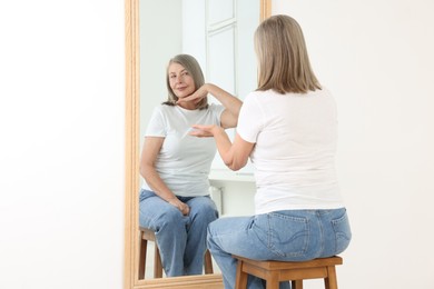 Image of Beautiful senior woman looking at herself in mirror indoors. Mental health