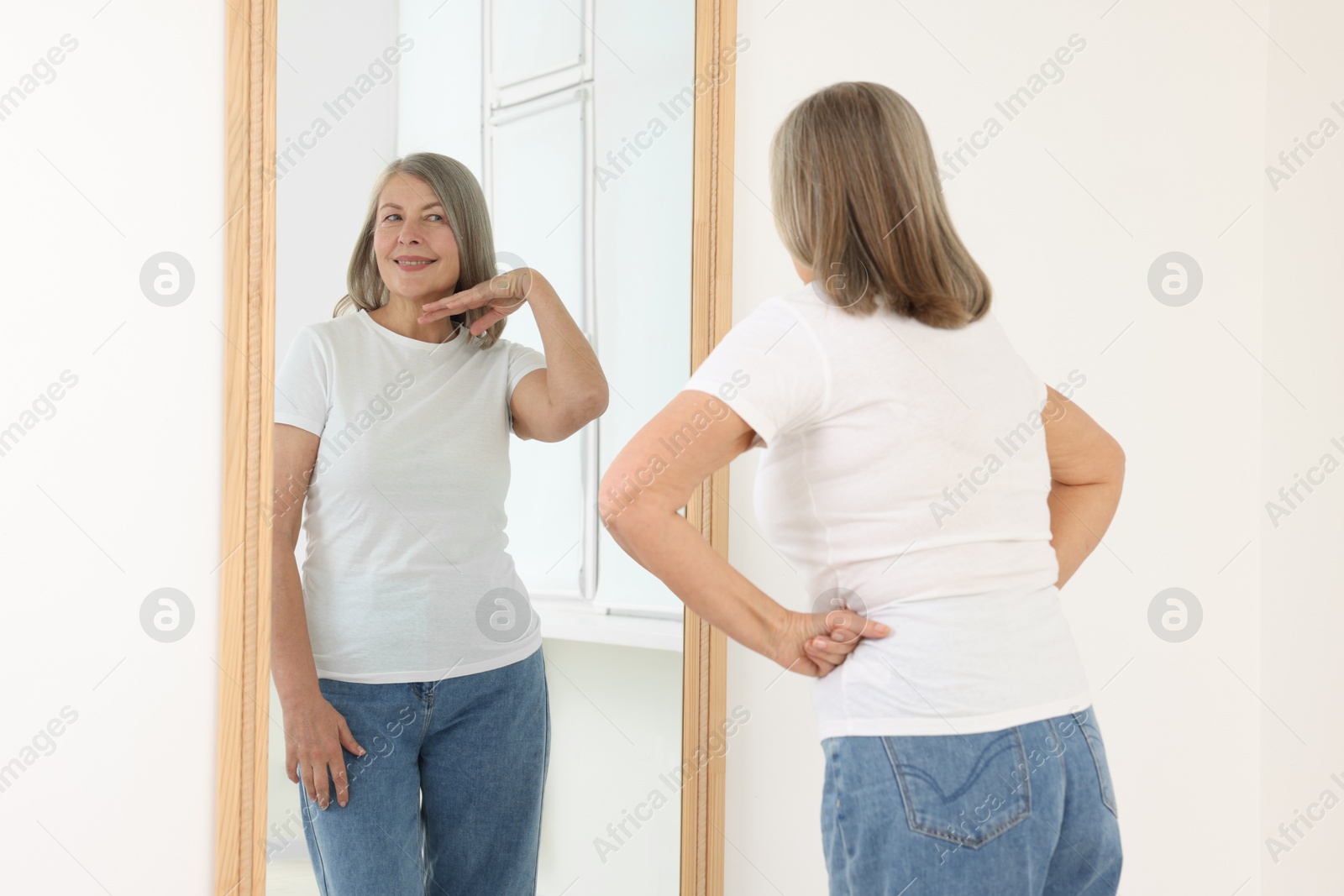 Image of Irritated senior woman looking at herself cheerful reflection in mirror indoors. Mental health