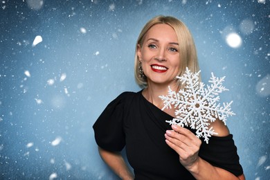 Image of Happy woman with beautiful makeup holding decorative snowflake against winter background
