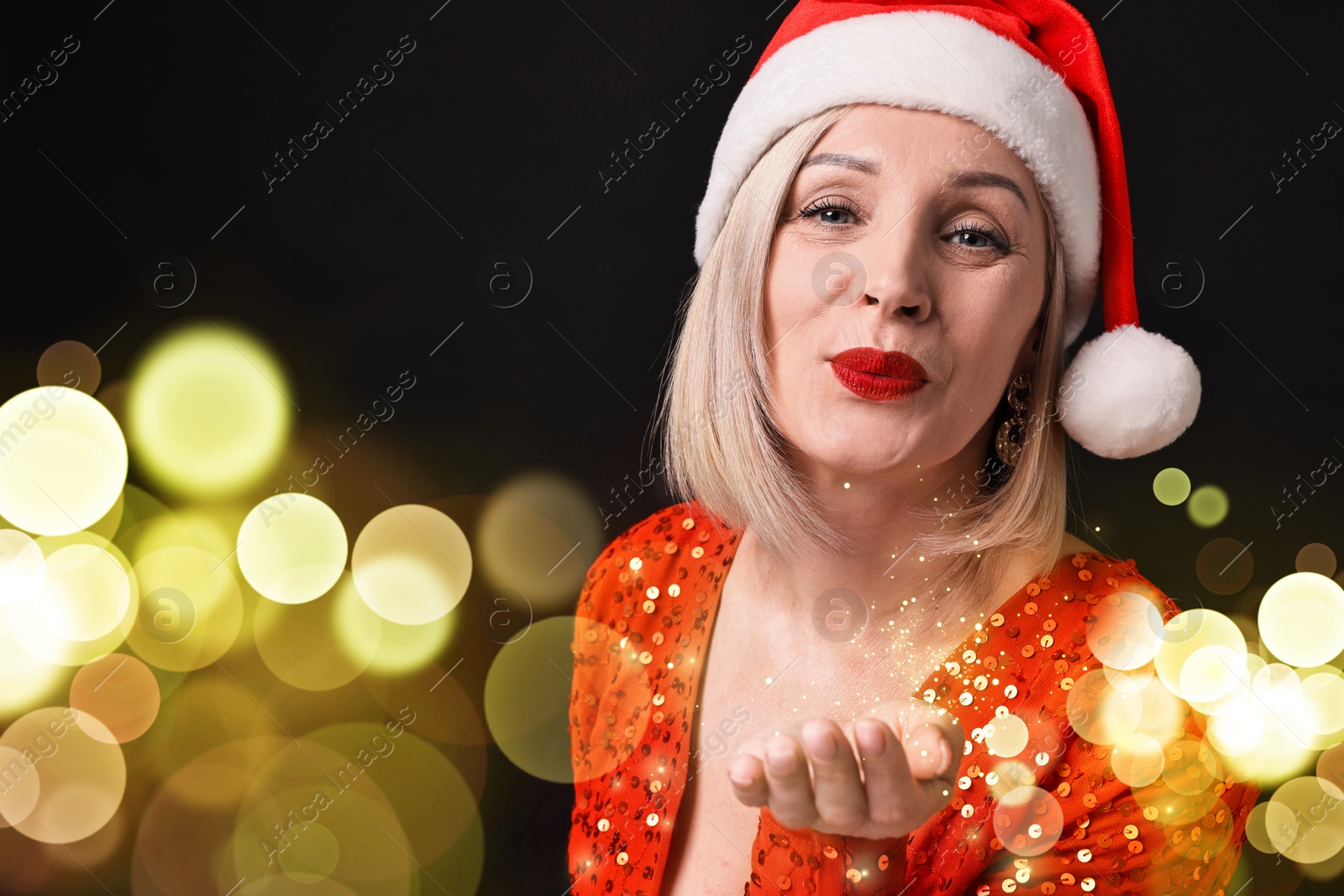 Image of Woman with perfect makeup in Santa hat sending air kiss on black background with bokeh lights