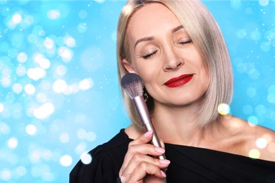 Image of Woman holding makeup brush on light blue background with bokeh lights