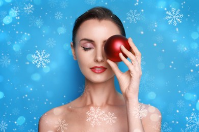 Image of Woman with perfect makeup holding Christmas bauble on light blue background with snowflakes