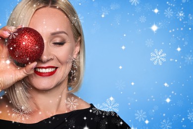 Image of Smiling woman with perfect makeup holding Christmas bauble on light blue background with snowflakes