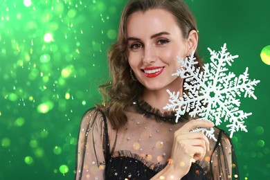 Image of Smiling woman with perfect makeup holding decorative snowflake on green background with bokeh lights