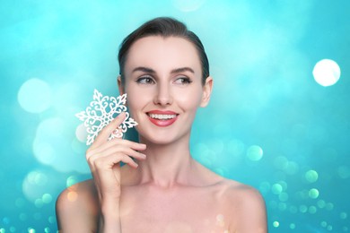 Image of Smiling woman with perfect makeup holding decorative snowflake on light blue background with bokeh lights