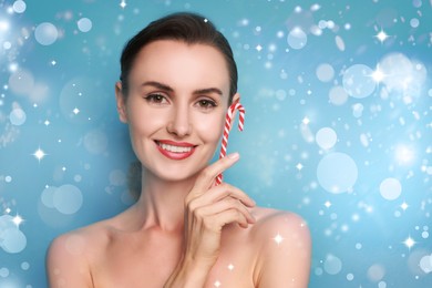 Image of Smiling woman with perfect makeup holding Christmas candy cane on light blue background with bokeh lights