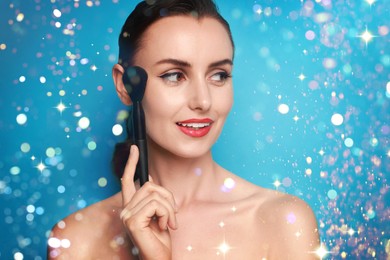 Image of Smiling woman holding makeup brush on light blue background with bokeh lights