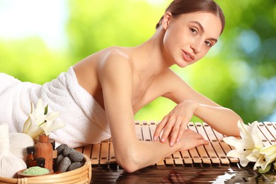 Image of Beautiful woman relaxing on bamboo mat against blurred green background. Spa center