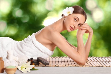 Image of Beautiful woman relaxing on bamboo mat against blurred green background. Spa center