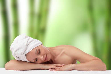 Image of Beautiful woman relaxing on towel against blurred green background. Spa center