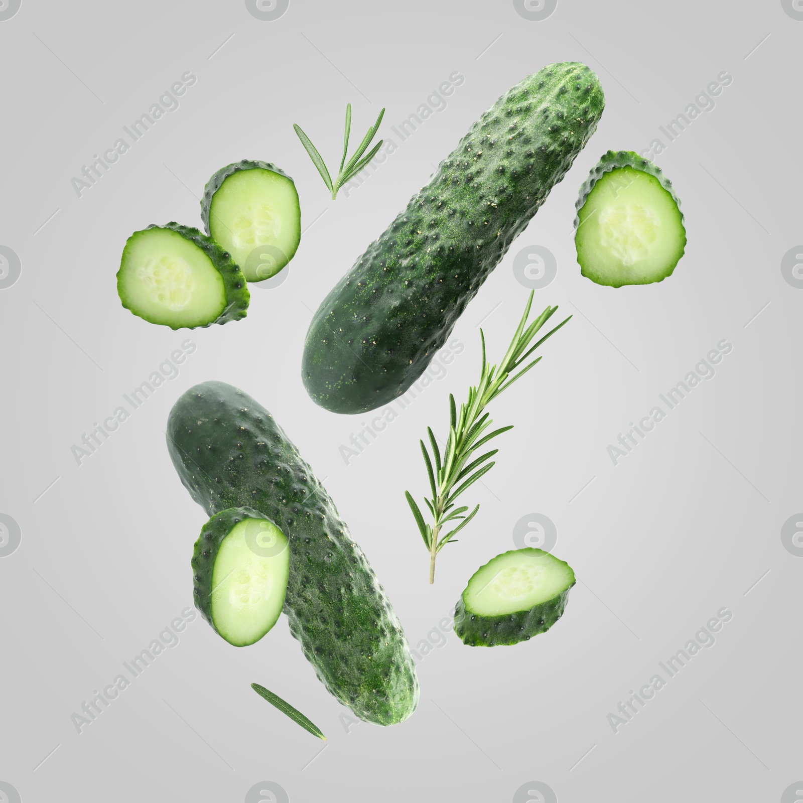 Image of Fresh cucumbers and rosemary falling against grey background