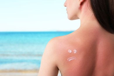 Image of Woman with sunburned skin against sea, back view. Smoothing cream on her shoulder