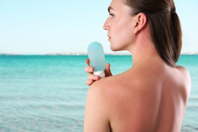 Image of Woman with sunburned skin holding smoothing cream against sea, back view