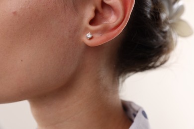 Photo of Woman wearing stylish earring on light background, closeup