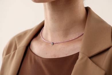 Photo of Woman wearing stylish necklace on light background, closeup