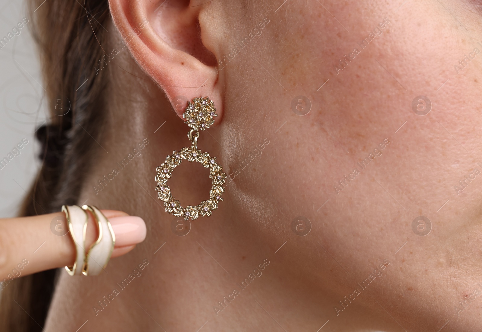 Photo of Woman wearing stylish earring and ring on light background, closeup