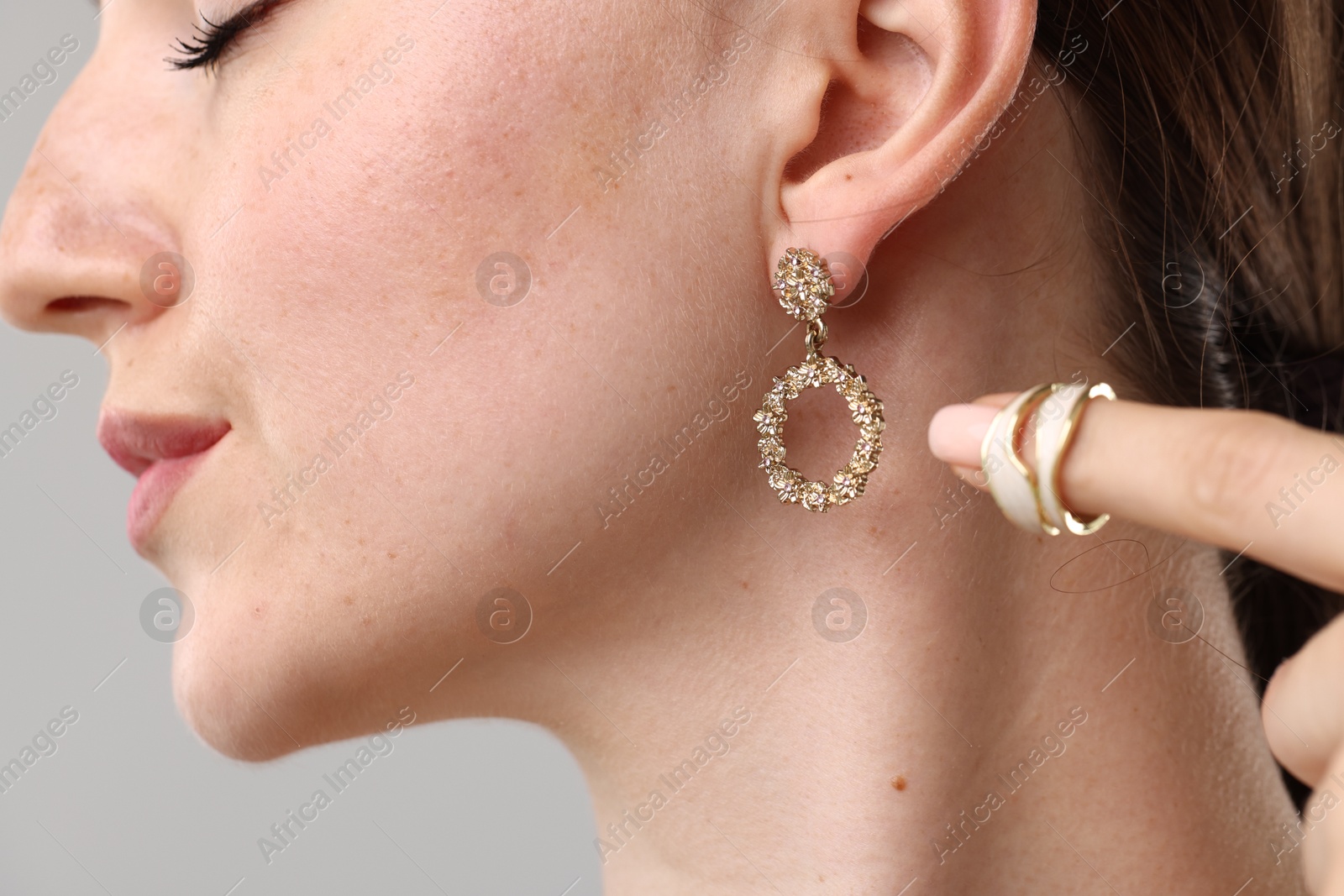 Photo of Woman wearing stylish earring and ring on light background, closeup