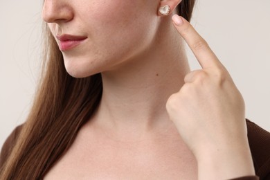 Photo of Woman pointing at her stylish earring on light grey background, closeup