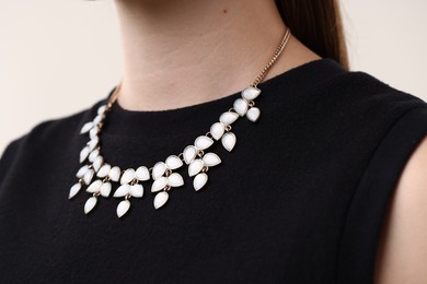 Photo of Woman wearing stylish necklace on light background, closeup