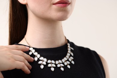 Photo of Woman wearing stylish necklace on light background, closeup