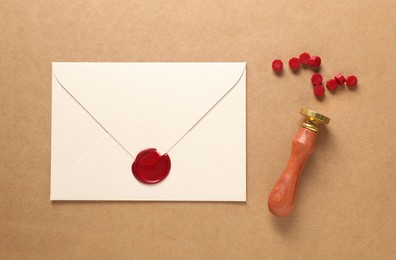 Photo of Beautiful wax stamp, sealing beads and envelope with seal on beige background, flat lay