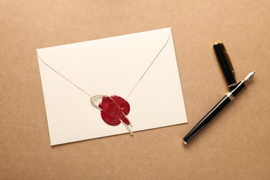 Photo of Beautiful envelope with wax seal, twine and fountain pen on beige background, flat lay
