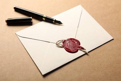 Photo of Beautiful envelope with wax seal, twine and fountain pen on beige background, closeup