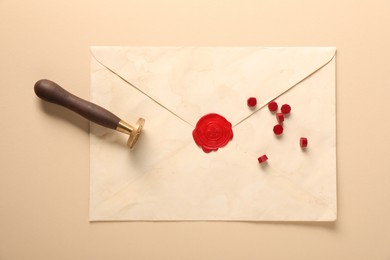 Photo of Beautiful wax stamp, sealing beads and envelope with seal on beige background, top view