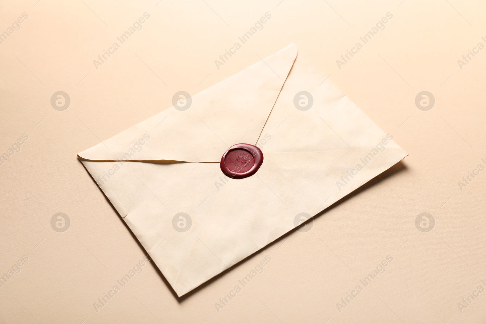 Beautiful envelope with red wax seal on beige background, closeup Photo of Beautiful envelope with red wax seal on beige background, closeup