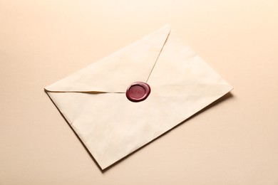Photo of Beautiful envelope with red wax seal on beige background, closeup