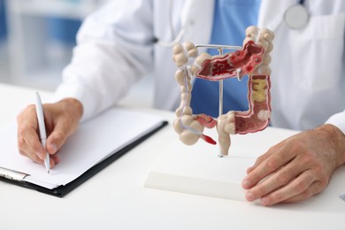 Photo of Gastroenterologist with model of large intestine working at white table in clinic, closeup