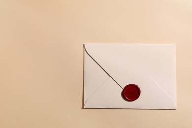 Photo of Beautiful envelope with red wax seal on beige background, top view. Space for text