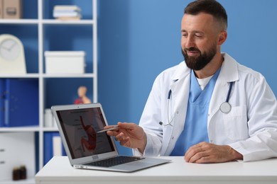 Photo of Gastroenterologist showing screen with illustration of stomach at table in clinic