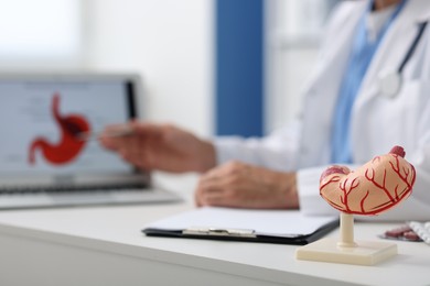 Photo of Gastroenterologist working at table in clinic, focus on human stomach model