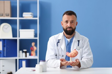 Photo of Gastroenterologist with model of stomach at white table in clinic