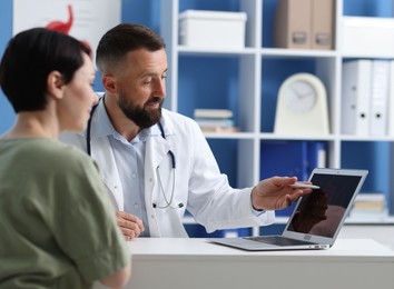 Photo of Gastroenterologist showing screen with illustration of digestive tract to patient at table in clinic