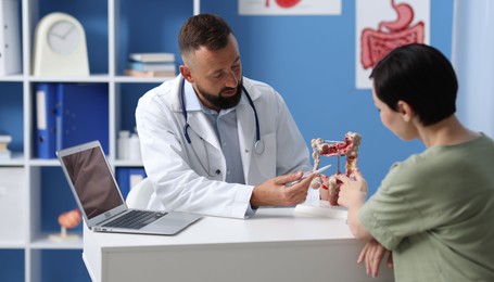 Photo of Gastroenterologist with model of large intestine consulting woman in clinic