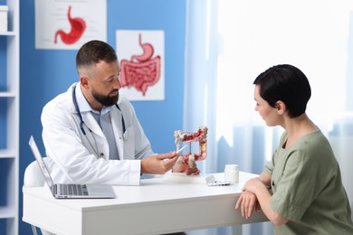 Photo of Gastroenterologist with model of large intestine consulting woman in clinic
