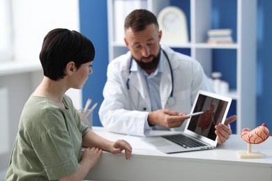 Photo of Gastroenterologist showing screen with illustration of large intestine to patient at table in clinic, selective focus