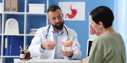 Photo of Gastroenterologist with model of stomach consulting woman in clinic