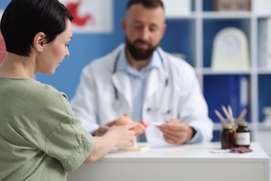 Photo of Gastroenterologist with model of stomach consulting woman in clinic, selective focus