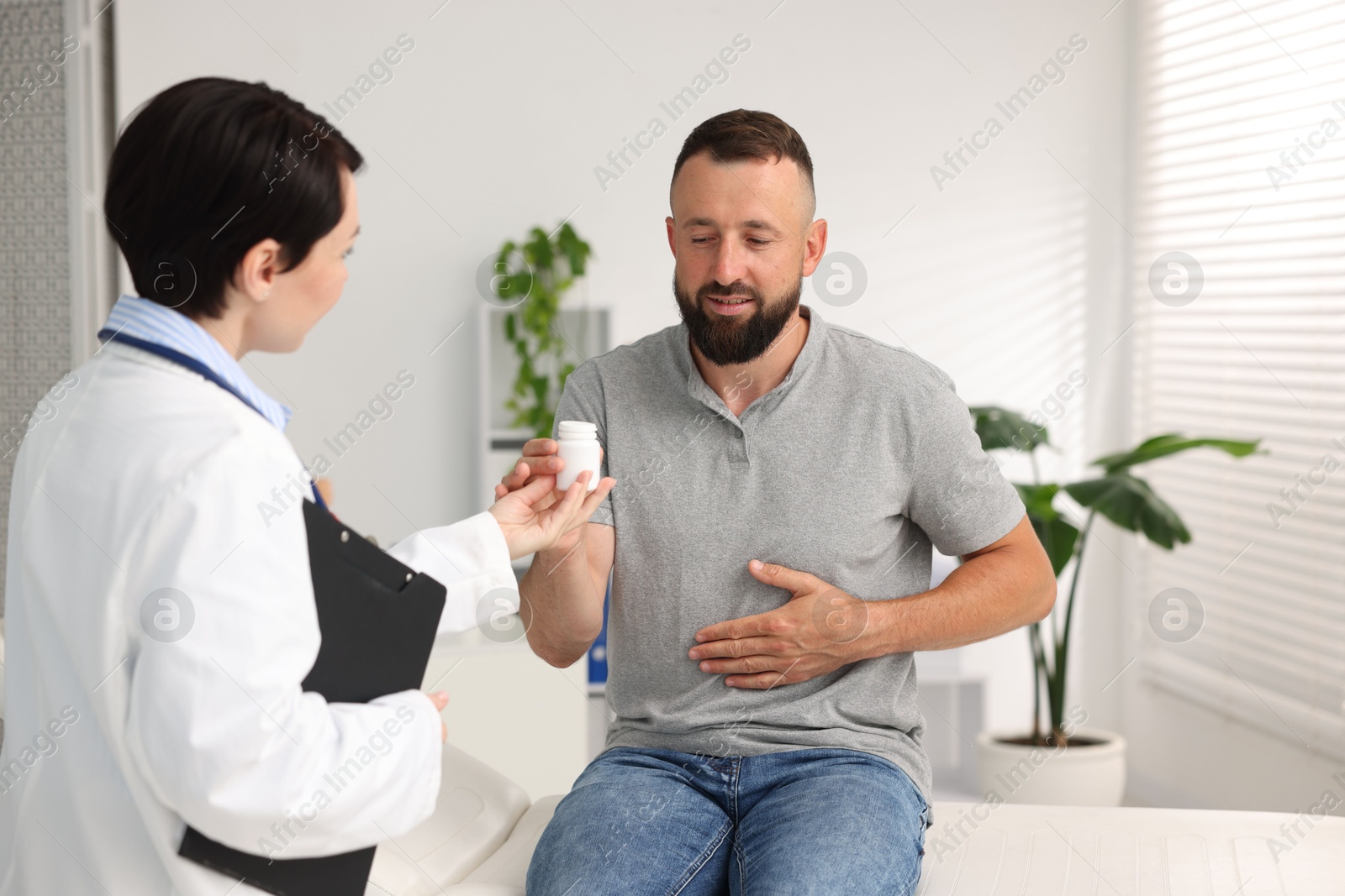 Photo of Gastroenterologist giving medical bottle with pills to patient in clinic