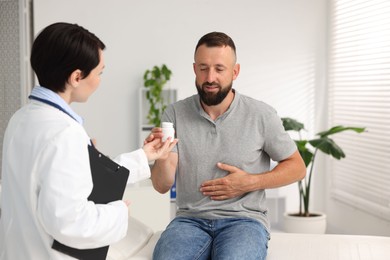 Photo of Gastroenterologist giving medical bottle with pills to patient in clinic