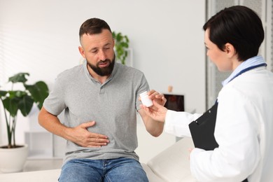 Photo of Gastroenterologist giving medical bottle with pills to patient in clinic