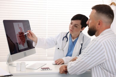 Photo of Gastroenterologist showing screen with illustration of digestive tract to patient at table in clinic