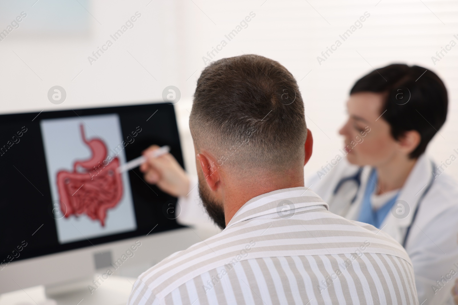 Photo of Gastroenterologist showing screen with illustration of digestive tract to patient at table in clinic, selective focus