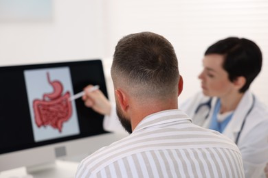 Photo of Gastroenterologist showing screen with illustration of digestive tract to patient at table in clinic, selective focus