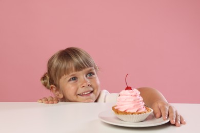 Photo of Cute little girl reaching for tasty dessert at white table against pink background