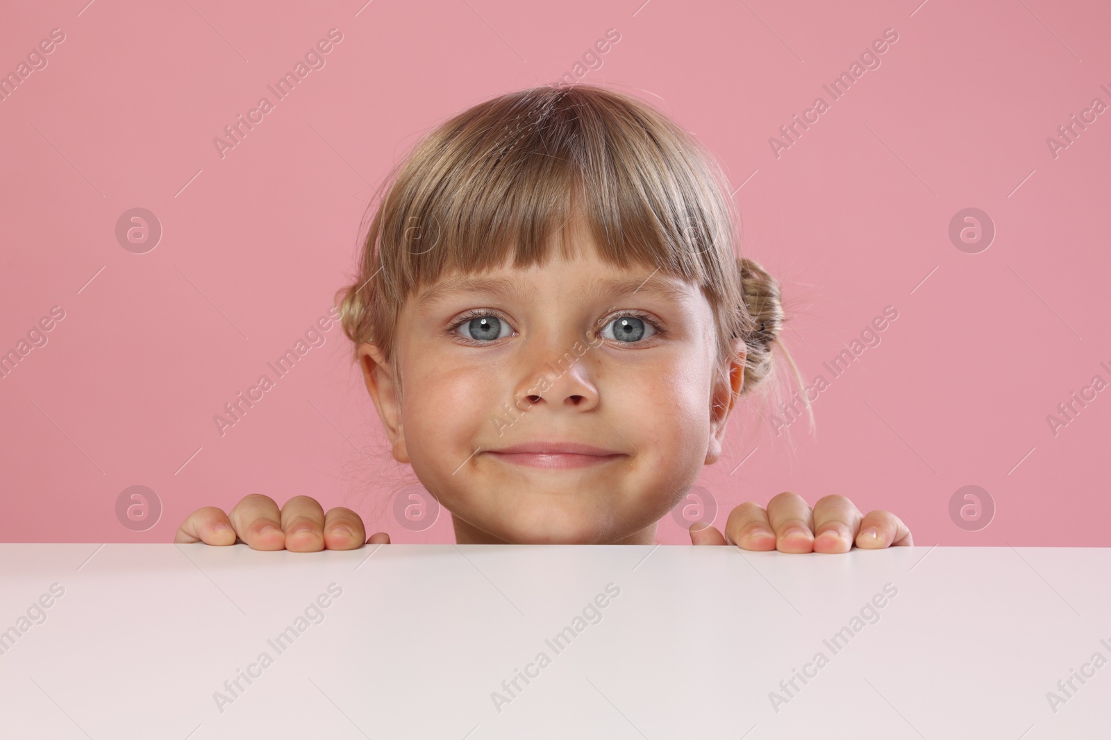 Photo of Curious little girl peeking over table against pink background