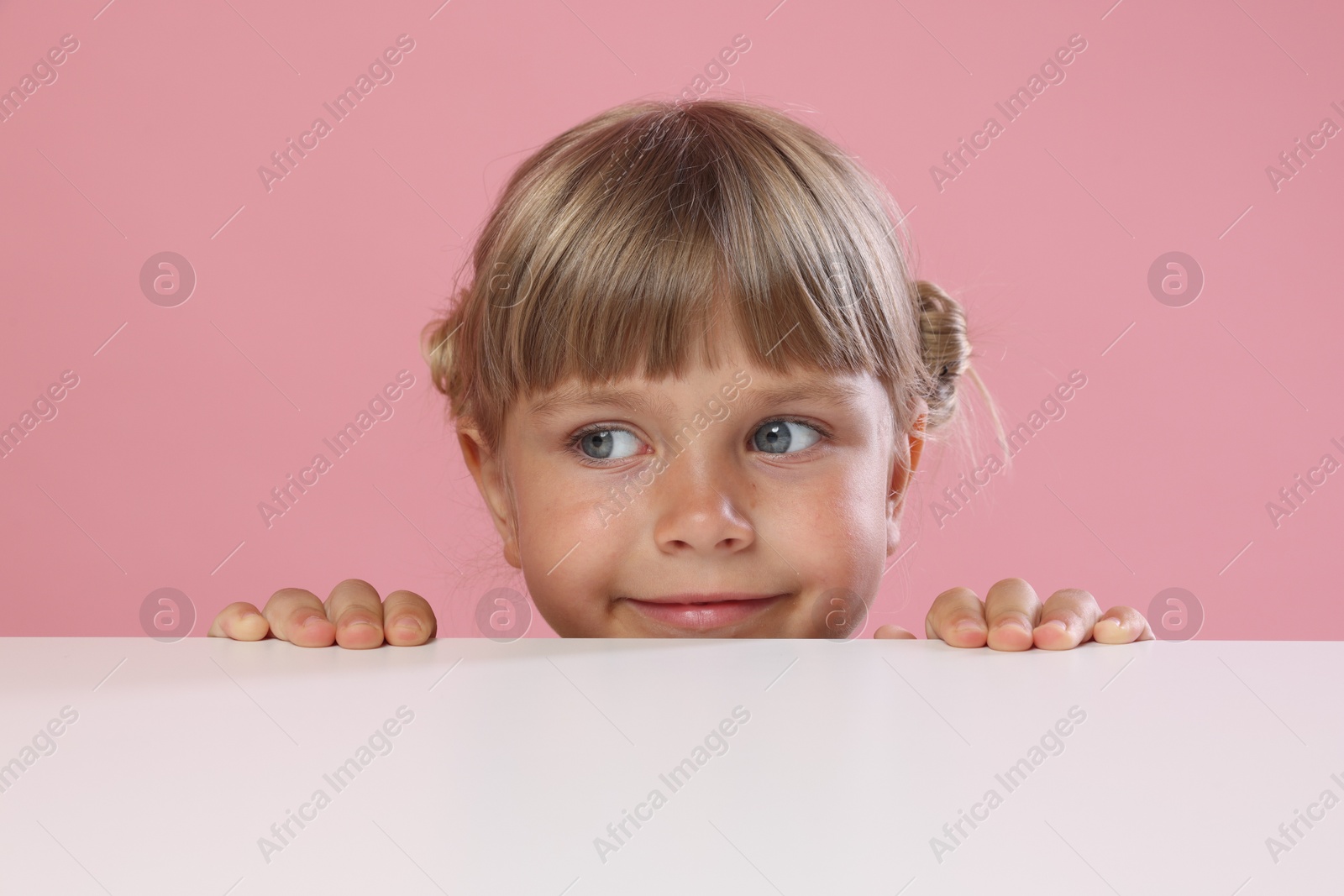 Photo of Curious little girl peeking over table against pink background